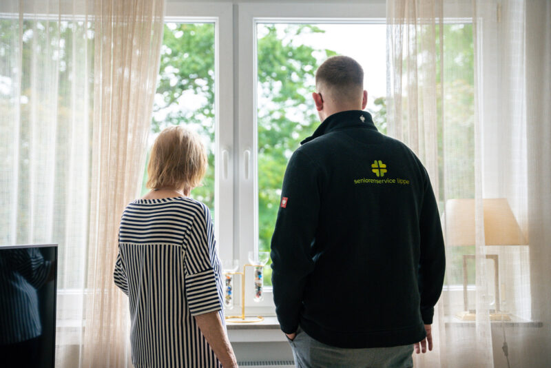Szene: Mitarbeiter des Seniorenservice steht mit einer Klientin am Fenster